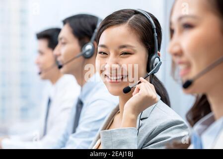 Smiling beautiful Asian woman working in call center office with team as customer service operators