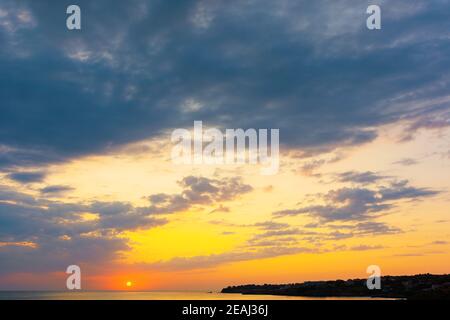 dynamic cloudscape in summer at sunrise. dark clouds on the sky in yellow and pink morning light. dramatic weather condition, picturesque scenery abov Stock Photo