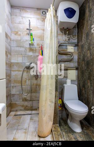 Small compact bathroom divided with shower curtain and toilet Stock Photo