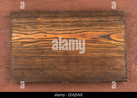 Rectangular board of dark wood lies on brown natural leather. Texture of a tree. Stock Photo