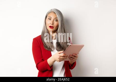Business. Surprised asian businesswoman looking impressed after reading something on digital tablet, standing over white background Stock Photo