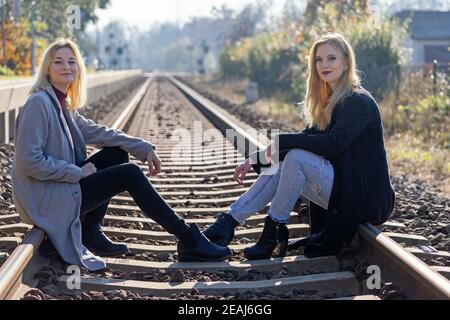 Two attractive young women  are sitting on rail and looking at the camera Stock Photo