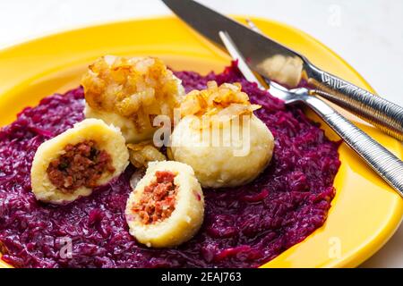 potato dumplings filled with smoked meat with fried onion on red cabbage Stock Photo