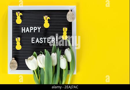 Easter bunny, flowers, and letter board on yellow background. Flat lay of Easter celebration concept. Stock Photo