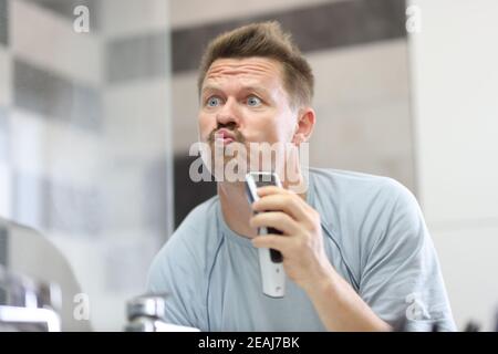 Man in front of a mirror shaves off his stubble with machine Stock Photo