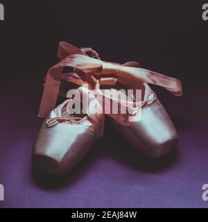 Pointe shoes ballet dance shoes with a bow of ribbons beautifully folded on a dark background. Stock Photo