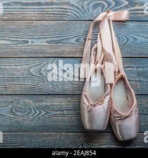 Pointe shoes ballet dance shoes with a bow of ribbons hang on a nail on a wooden background. Stock Photo