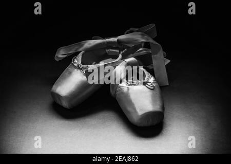 Pointe shoes ballet dance shoes with a bow of ribbons beautifully folded on a dark background. Stock Photo