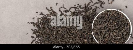 Dried tea is poured into a white ceramic cup on a gray textured background. View from above. Layout. Stock Photo