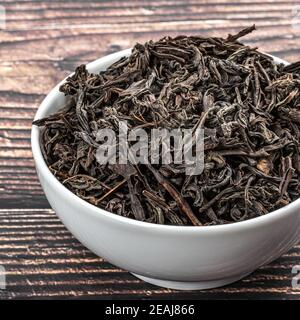 Dried tea is poured into a ceramic cup on a wooden plank table. Stock Photo