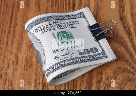 On a wooden table, American dollar bills are rolled up and clamped with a paper clip. Stock Photo