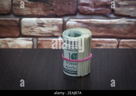 a bundle of American dollar bills of one hundred dollars on a wooden table near a brick wall. Stock Photo