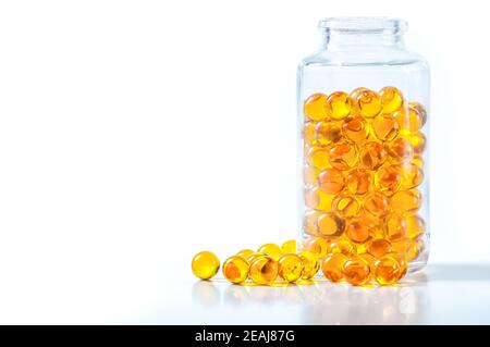 Yellow capsules scattered from a glass jar on a white background. Stock Photo