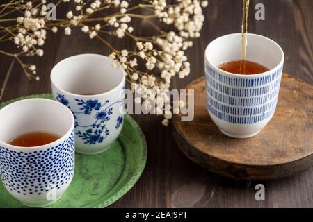 View of three blue cups with tea, white flowers, selective focus, on green plate and wooden table, horizontal Stock Photo