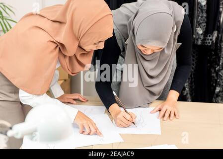Muslim woman fashion designer drawing dress sketches working together with her colleague in tailor shop Stock Photo