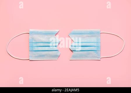 Protective surgical mask split in two on pink background.Concept of protesting against coronavirus scams Stock Photo