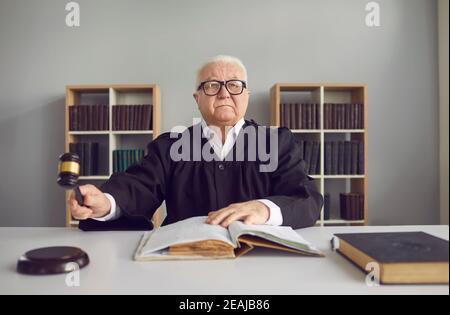 Senior man professional judge sitting in conference hall during trial and striking with hammer Stock Photo