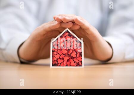 Wooden house with many red hearts protected by hands Stock Photo