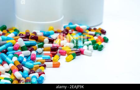 Colorful capsule pills near plastic drug bottle. Multi-colored capsule pills on white table. Pharmacy drugstore products. Pharmaceutical industry. Health budget and policy. Bright color capsule pills. Stock Photo