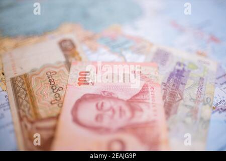 50 kyat bill, 100 baht bill, and a 100 riels bill on a map of Southeast Asia Stock Photo