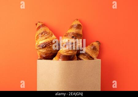 A croissant protruding from a paper bag placed on an orange background Stock Photo