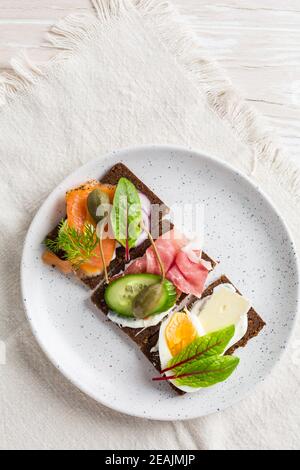 Variation of healthy open sandwiches on Pumpernickel bread with vegetables, salmon, ham, herbs and soft cheese Stock Photo