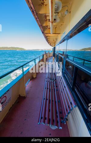 The Sydney Harbour foreshore is reflected in the side windows of a Manly Ferry as it makes its way down the harbour towards Manly Stock Photo