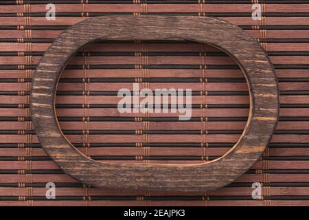 Beautiful wooden frame cut from a solid dark board, lies on a dark bamboo mat. Stock Photo
