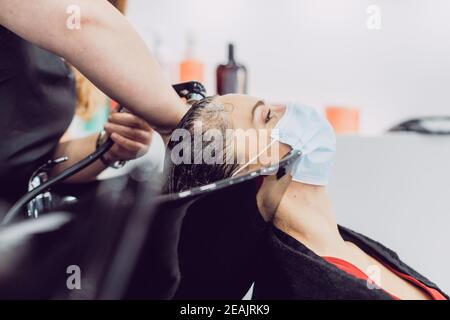 Woman with face mask in a hair salon during har wash Stock Photo