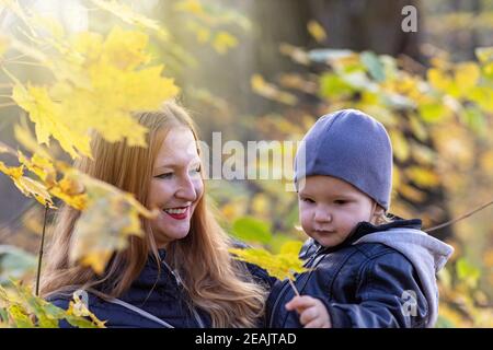 Young red haired mother and her son posing under maple tree outdoors closeup. Stock Photo