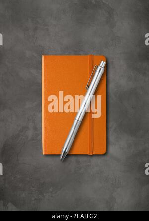 Orange closed notebook with a pen on dark concrete background Stock Photo