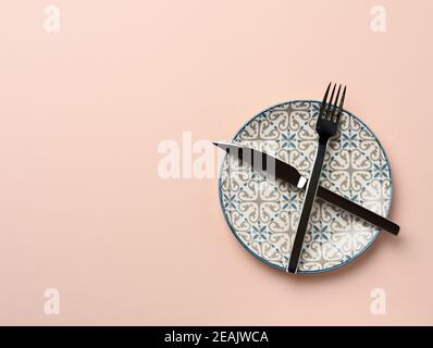 round ceramic plate and crossed knife and fork on beige background Stock Photo