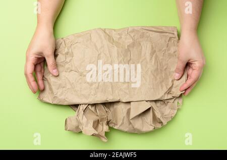 two hand holds piece of crumpled brown paper on a green background Stock Photo