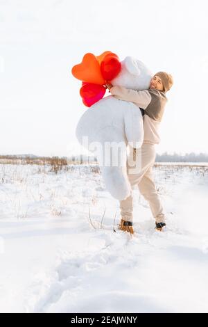 Candid millennial man holding big teddy bear soft toy gift heart air balloons on this special day surprising wife. romantic present for Birthday, Chri Stock Photo