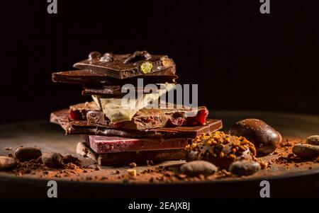 Stack of assorted chocolate with cocoa and cocoa beans on black background Stock Photo