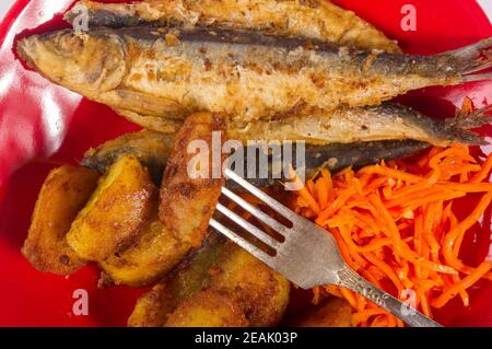 Homemade dish - fried potato wedges with small fish and pickled carrots on a red plate, simple rustic food, close-up Stock Photo
