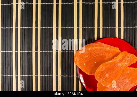 Large slices of dried mango in a red saucer on a bamboo mat, close up. Stock Photo