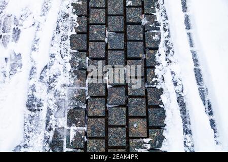 Stone path in the park in the snow close-up. Winter in the city. Stock Photo