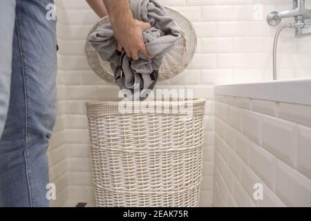 Man puts used dirty clothes in a dirty laundry basket. Stock Photo