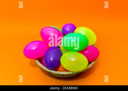 Wicker basket with colorful Easter eggs on yellow paper background. Stock Photo