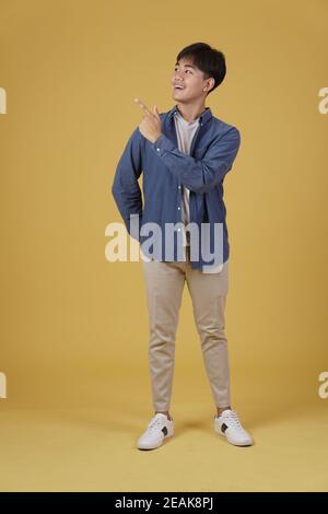 portrait of happy handsome young asian man dressed casually pointing fingers at copyspace isolated on yellow studio background Stock Photo