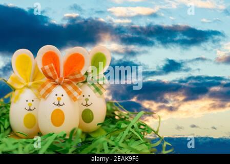 Decorated easter eggs, three bunnies on grass over blue sky sunset cloudy evening background. Happy Easter. Stock Photo