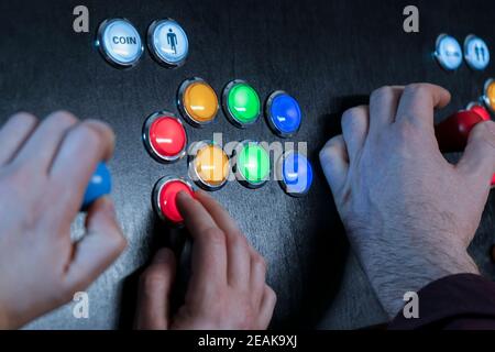Closeup view of two people hands playing arcade vintage video games.Gamepad with joystick and many colorful buttons .Gaming concept. Stock Photo