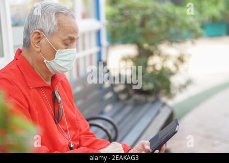 asian old elder senior man elderly male wearing face mask using mobile smart phone cellphone outdoor. mature retirement lifestyle Stock Photo