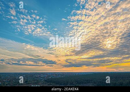 beautiful yellow-blue sky with clouds and overcast at sunset over a large dense forest and town Stock Photo
