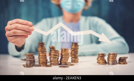 Woman holding an arrow down over stack of coins. Stock Photo