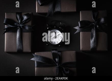 gift box wrapped in black paper and black bow ribbon and black alarm clock Stock Photo