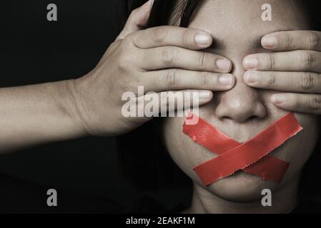 Asian woman blindfold wrapping mouth with red adhesive tape Stock Photo