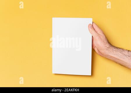 Male hand holding a closed book-catalog with blank cover on yellow background mock-up series 270 Stock Photo