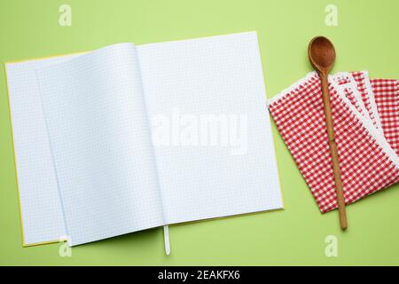 open notebook with blank white sheets and wooden spoon on green background Stock Photo